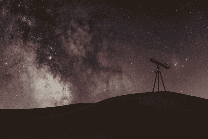 Telescópio em tripé em silhueta sob céu estrelado com a Via Láctea, cenário de astrofotografia para iniciantes.