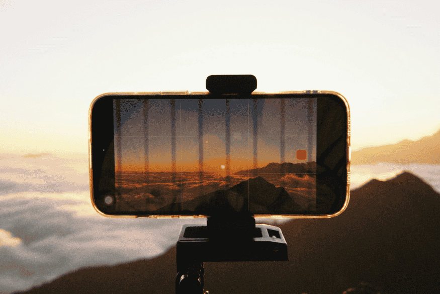 Smartphone preso em suporte fotografando horizonte montanhoso ao amanhecer, mostrando acessório útil para capturar imagens com mais estabilidade.