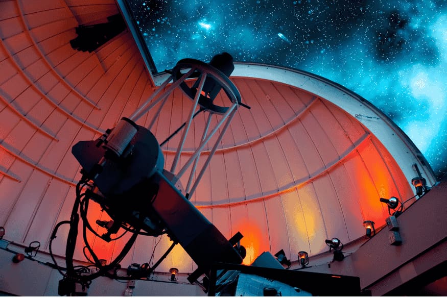 Telescópio em observatório com cúpula aberta e céu estrelado ao fundo, cenário típico de eventos de observação astronômica guiados.