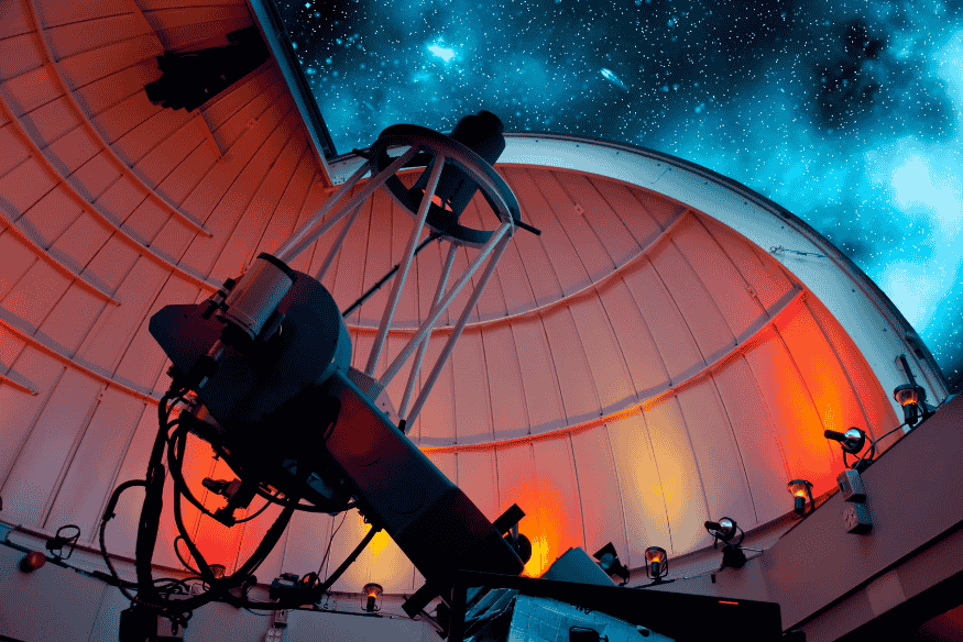 Telescópio dentro de observatório apontado para o céu estrelado, utilizado na observação de estrelas variáveis.