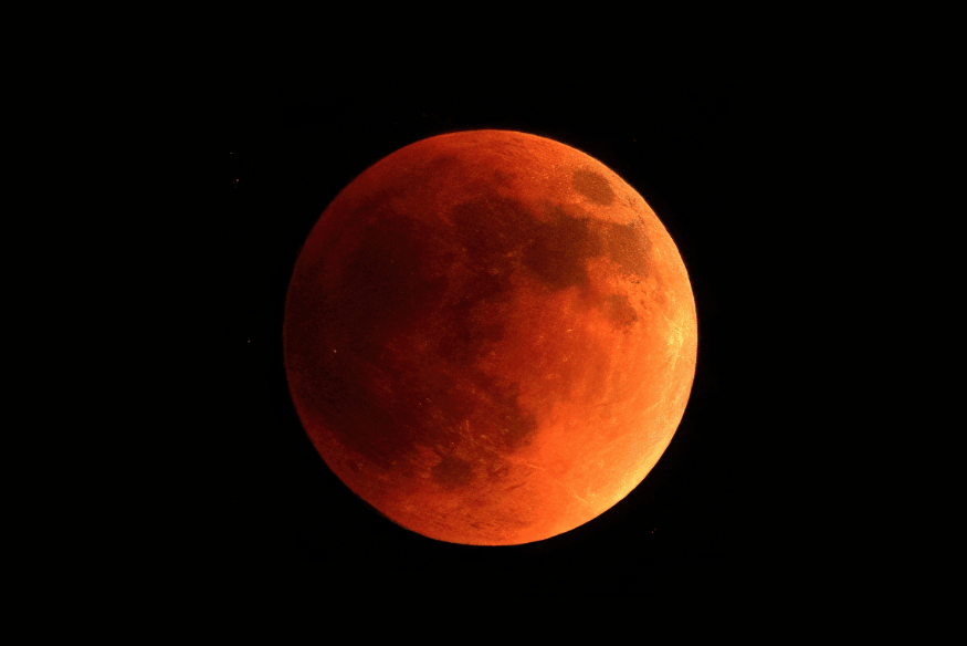 Lua avermelhada durante eclipse lunar total, conhecida como “Lua de sangue”, com detalhes da superfície visíveis.
