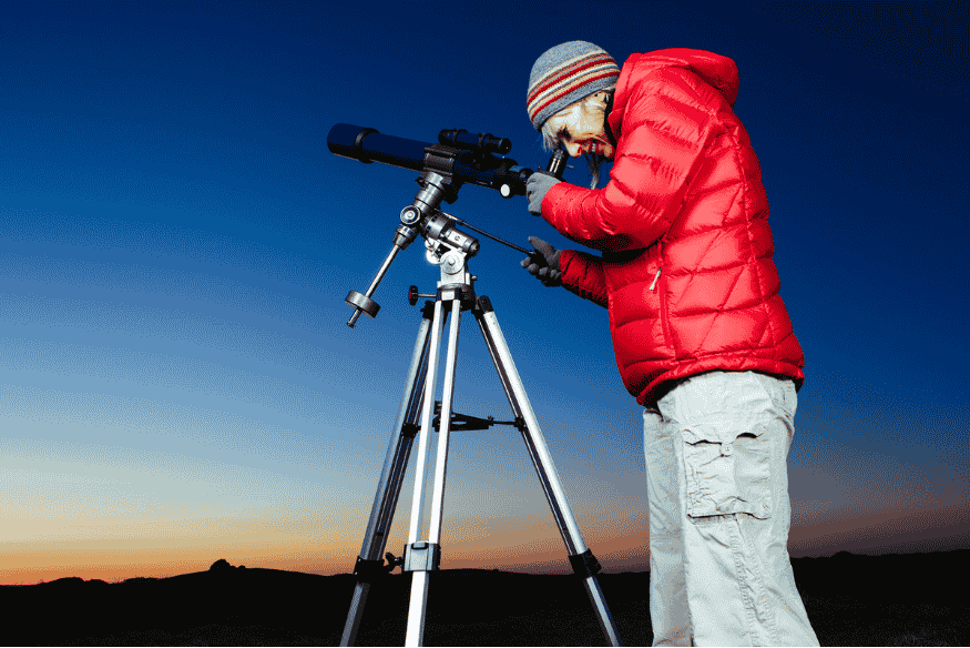 Pessoa ajustando telescópio ao ar livre no início da noite, preparação importante para observar e fotografar eclipses com cuidado.