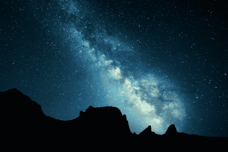 Via Láctea brilhando no céu noturno sobre montanhas em silhueta, exemplo de fotografia astronômica para iniciantes.