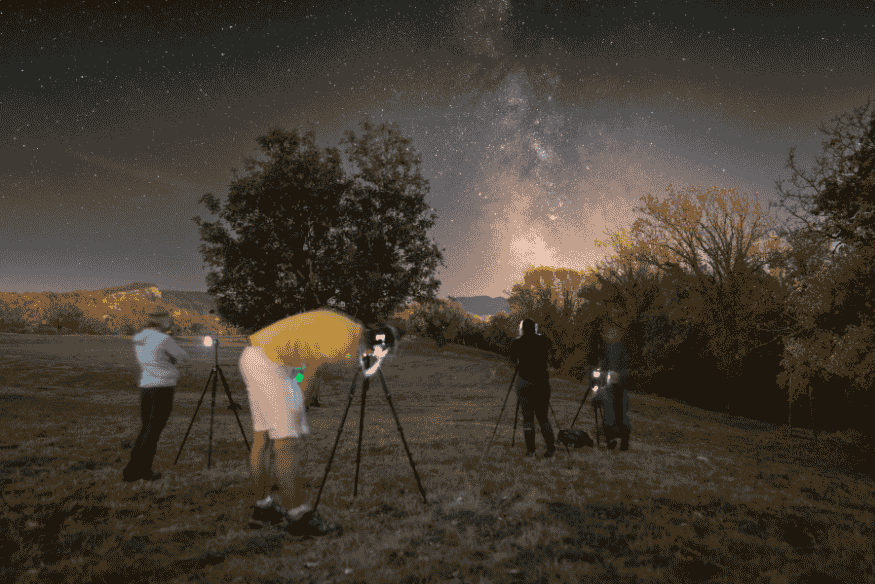 Grupo de pessoas fotografando a Via Láctea em campo aberto à noite com tripés e câmeras voltadas para o céu.