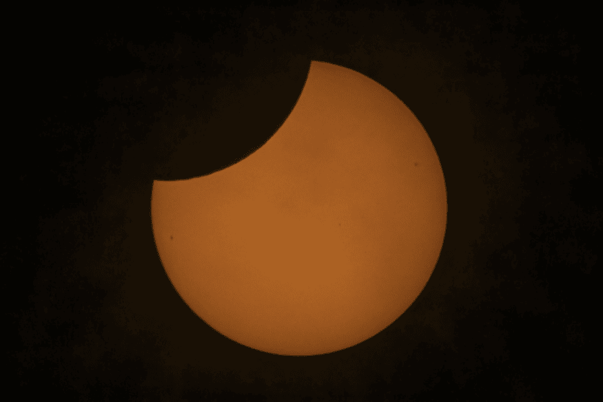 Eclipse solar parcial com o Sol alaranjado parcialmente encoberto, ilustrando fenômenos de eclipses ao longo da história.