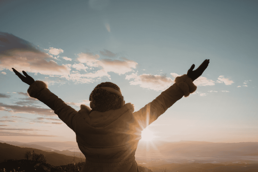 Pessoa de costas com braços abertos ao nascer do sol, ilustrando como a luz natural influencia o corpo humano e o bem-estar.