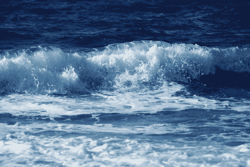 Close de ondas quebrando no mar com espuma e água em movimento, representando a força e a dinâmica das marés.