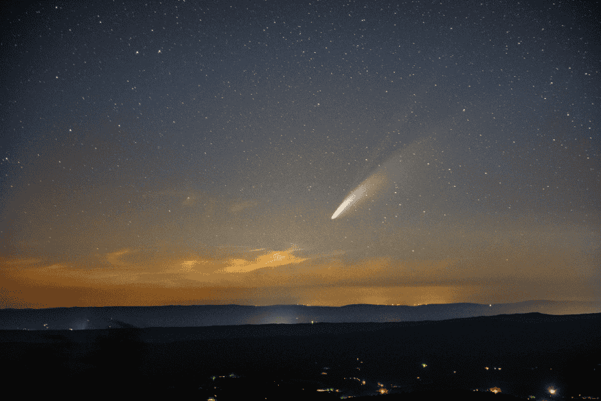 Céu noturno com cometa ou meteoro brilhante e cauda sobre o horizonte, ideal para ilustrar observação de meteoros.