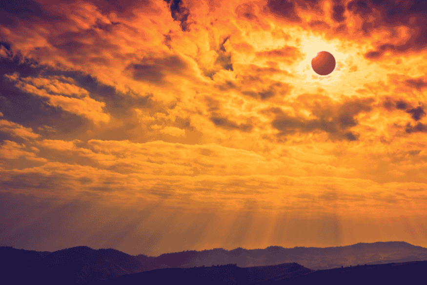 Eclipse solar visto em céu alaranjado com nuvens e raios de luz, mostrando o disco escuro próximo ao Sol.