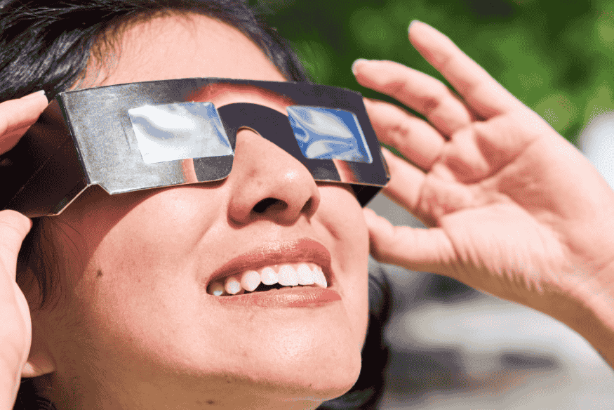 Pessoa usando óculos de eclipse solar de papel com filtros escuros, ajustando a armação enquanto observa o céu.