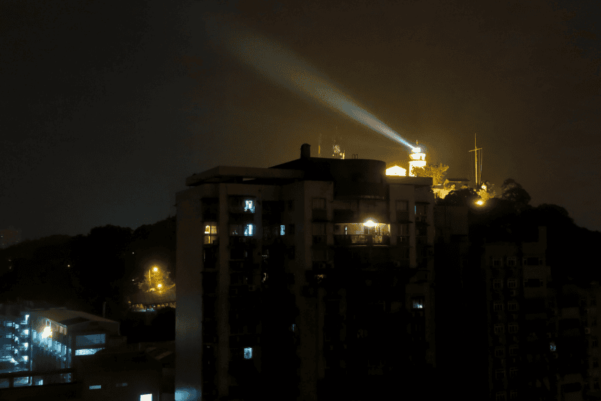 Facho de luz artificial iluminando o céu noturno sobre prédios, exemplo claro de poluição luminosa em áreas urbanas.