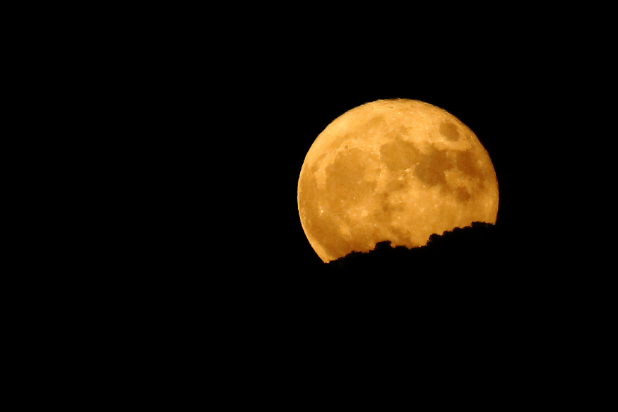 Superlua alaranjada no céu noturno com recorte na borda inferior, destacando o maior brilho do ano.