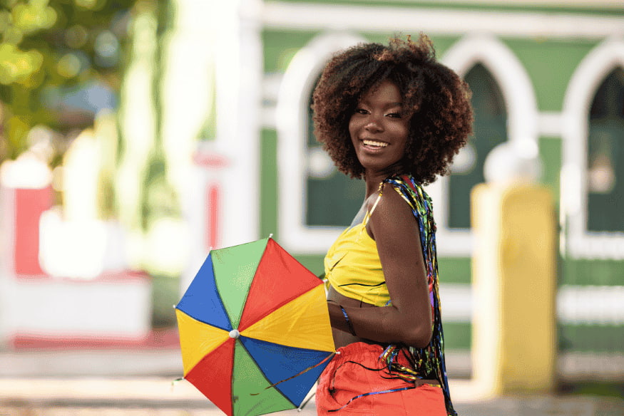 Mulher sorridente segurando sombrinha de frevo durante o carnaval.