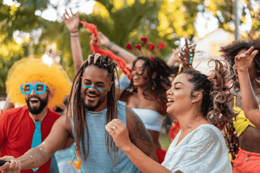 Grupo de amigos fantasiados dançando e se divertindo ao ar livre durante o carnaval.