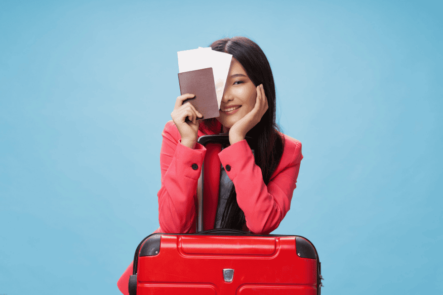 Mulher sorrindo segurando passaporte e passagens com mala vermelha