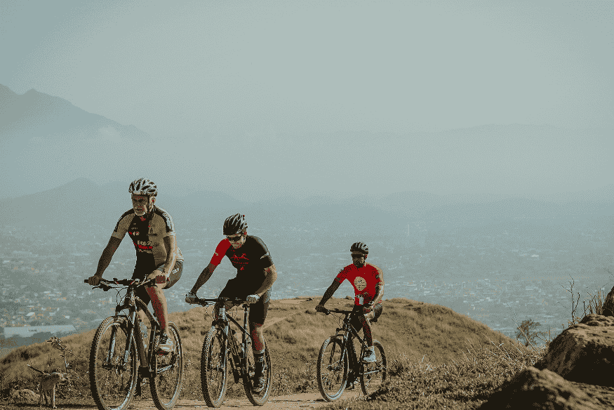 Três ciclistas pedalando em trilha elevada com vista para o Vale Europeu, Santa Catarina.