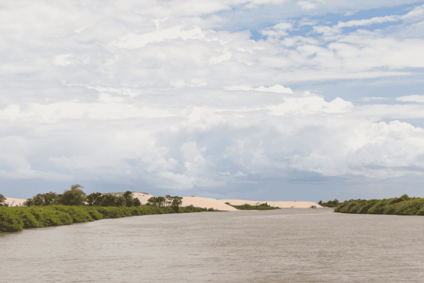 Vista ampla do rio com vegetação e dunas ao fundo no Delta do Parnaíba