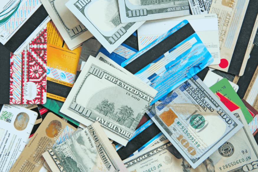 Cédulas de dólar e diversos cartões de crédito e débito espalhados sobre uma superfície