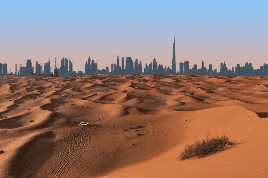 Vista panorâmica do deserto de Dubai com a cidade ao fundo durante o pôr do sol