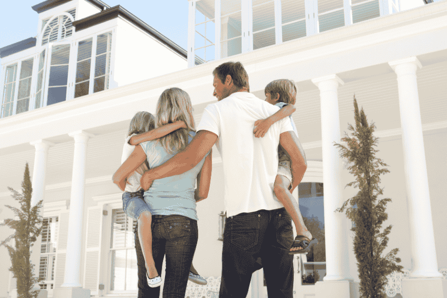 Família com duas crianças observando a fachada de uma casa grande e moderna.