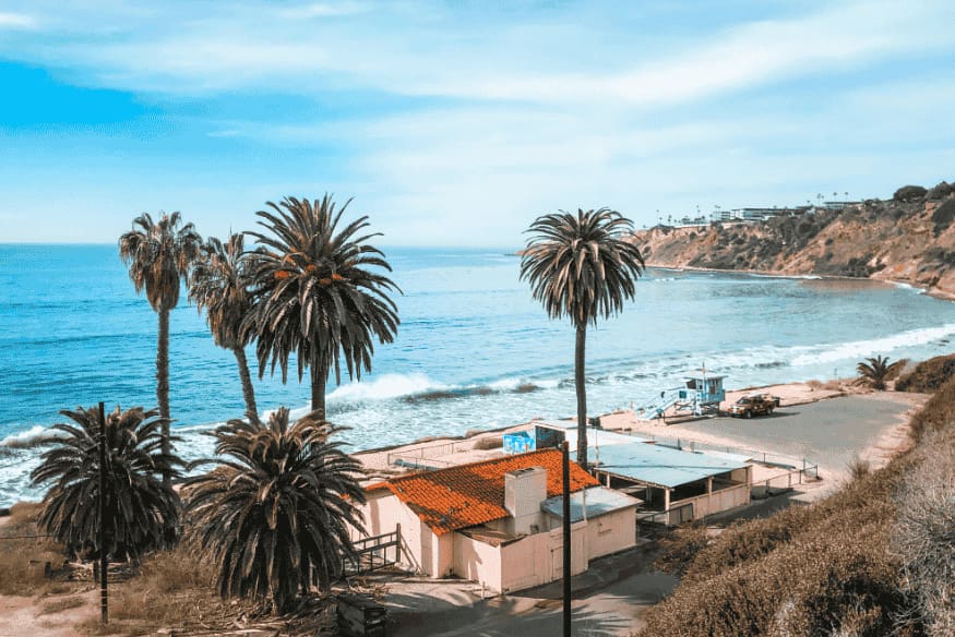Casa de temporada à beira-mar com coqueiros ao redor e vista para o oceano.