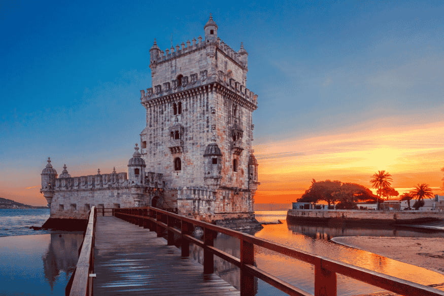 Torre de Belém em Lisboa iluminada pelo pôr do sol, com passarela sobre o rio Tejo