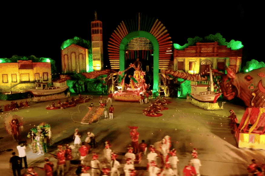 Arena do Festival de Parintins com alegorias do Boi Garantido em tons vermelhos e verdes.