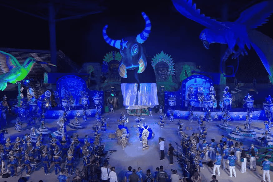 Apresentação da galera do Boi Garantido em arena, com alegorias azuis e grandes esculturas iluminadas.
