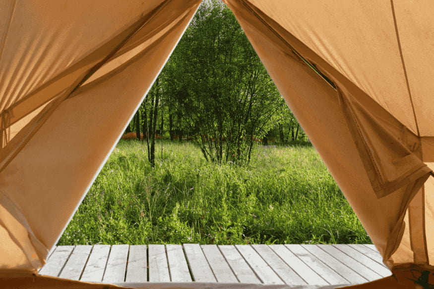 Vista da área verde através da abertura de uma barraca de glamping