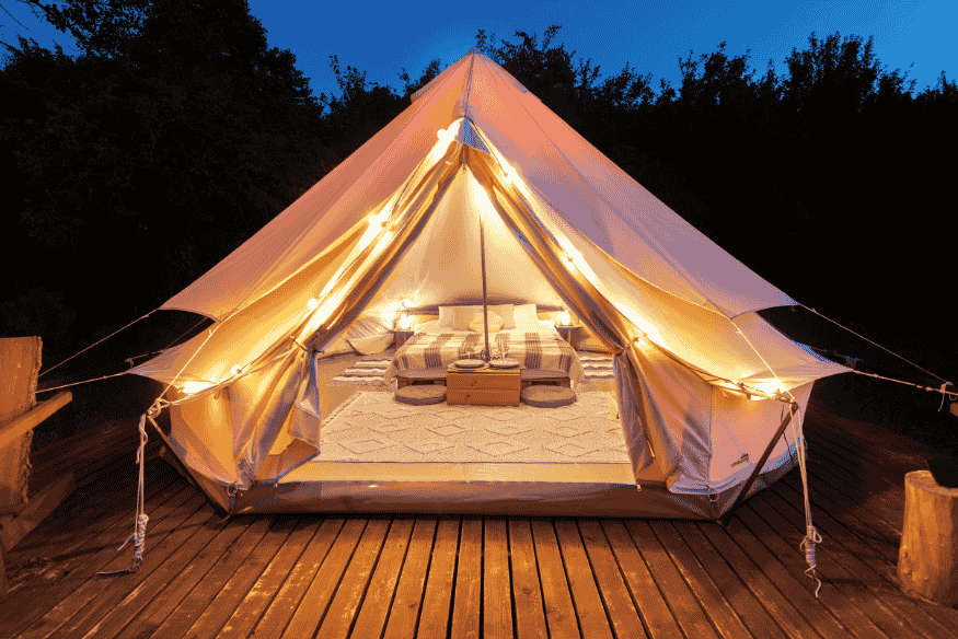 Interior de barraca de glamping decorado com cama confortável e luzes