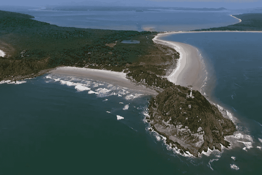 Vista aérea do Farol das Conchas na ponta da Ilha do Mel, cercado por vegetação e praias desertas.