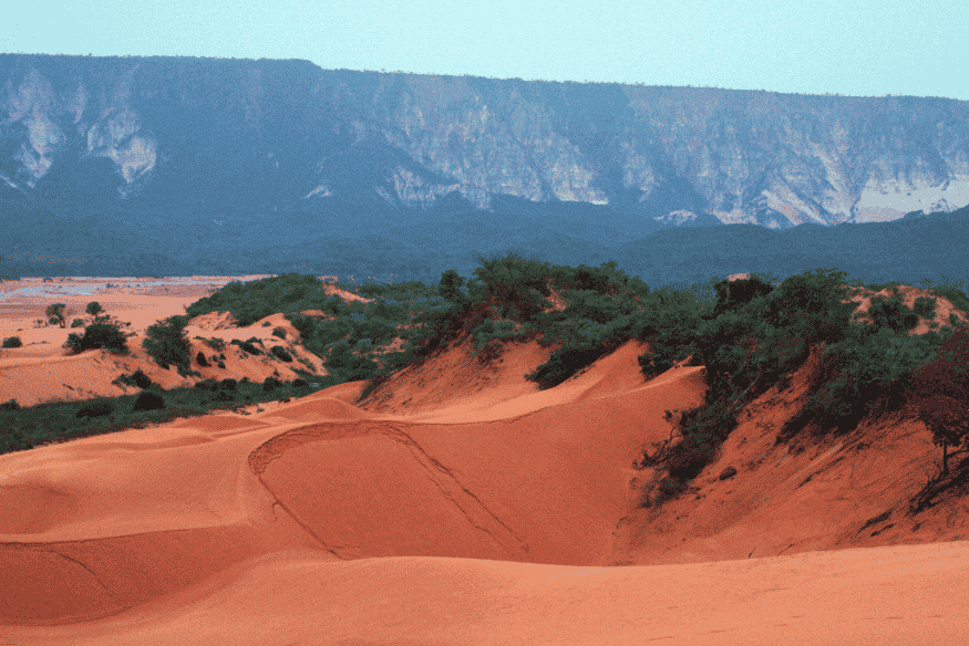 Dunas avermelhadas do Jalapão com vegetação esparsa e serra ao fundo