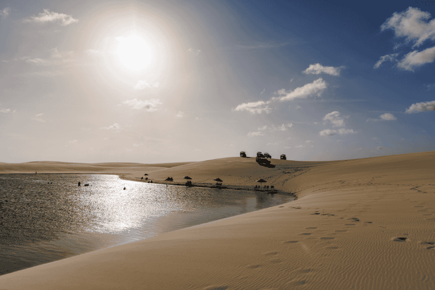 Lagoa entre dunas ao pôr do sol nos Lençóis Maranhenses com visitantes e veículos