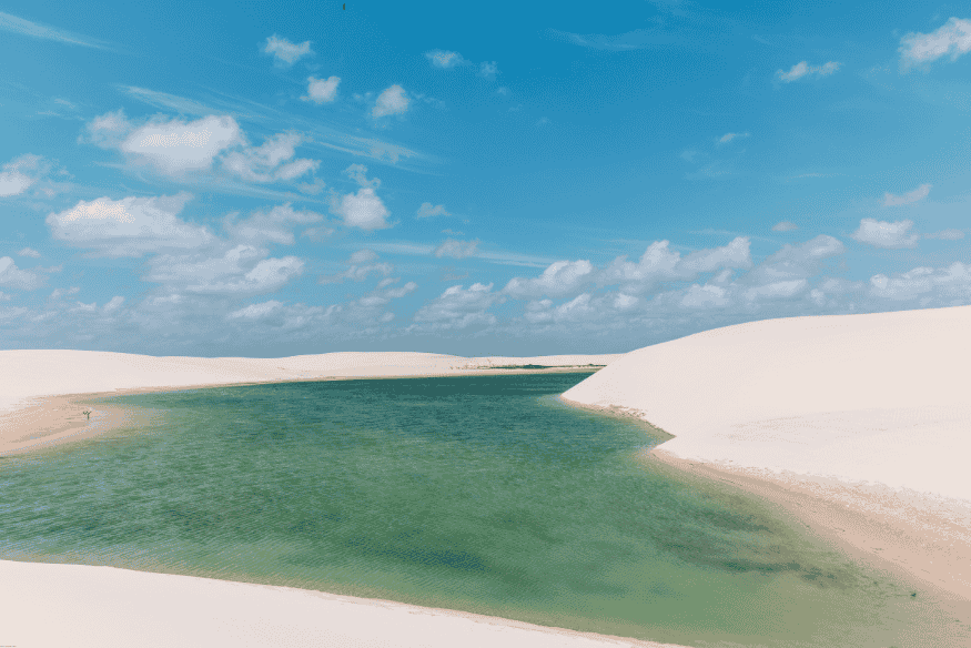 Lagoa de água verde entre dunas brancas sob céu azul nos Lençóis Maranhenses