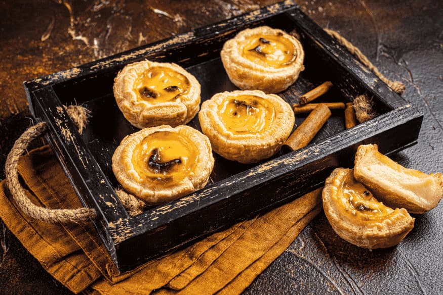 Pastéis de nata tradicionais em bandeja rústica com pau de canela ao lado