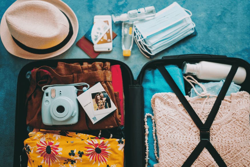 Itens organizados em uma mala cápsula com roupas, câmera, chapéu e acessórios para viagem