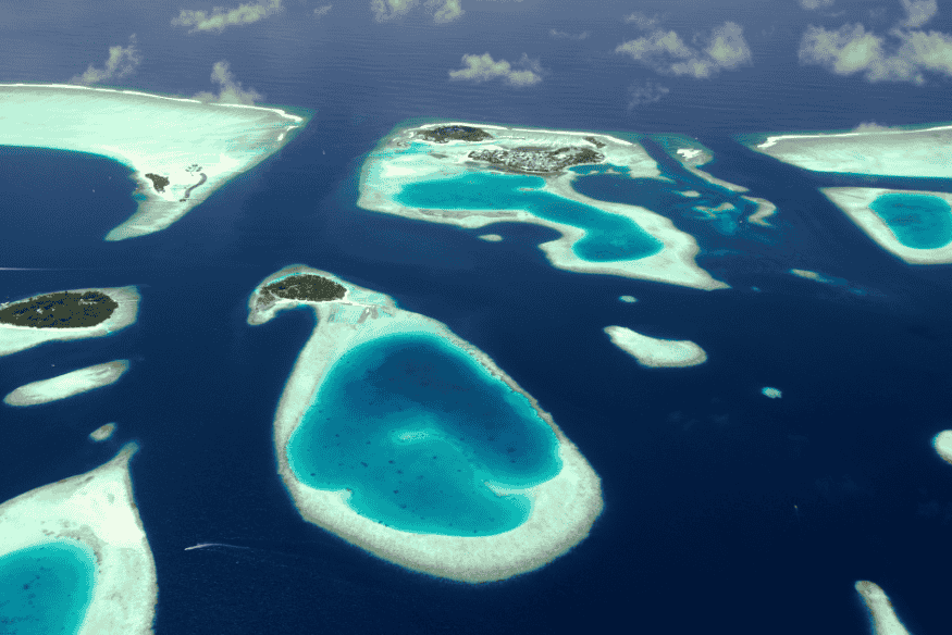 Vista aérea de vários atóis e ilhas nas Maldivas cercadas por águas cristalinas e recifes de corais.