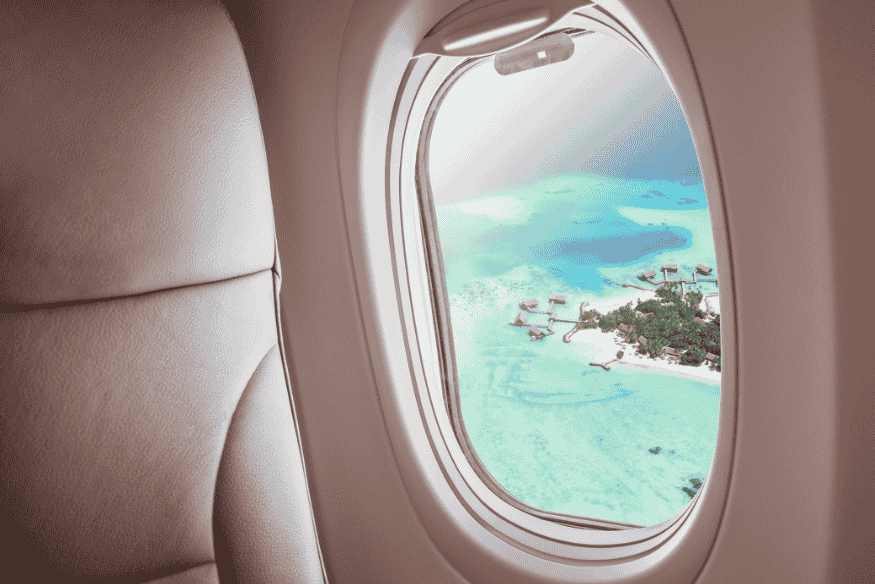 Vista de uma ilha das Maldivas pela janela do avião, destacando bangalôs sobre águas azul-turquesa.