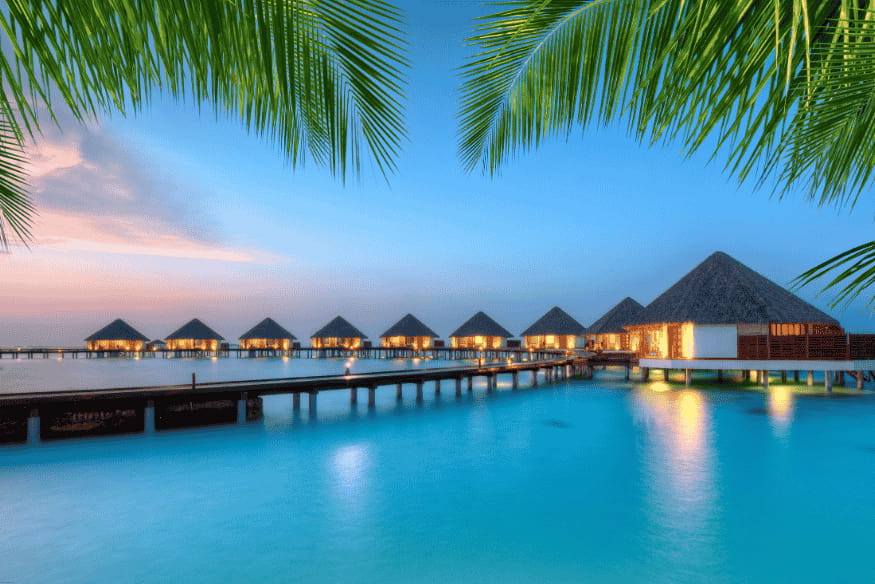 Bangalôs sobre o mar ao pôr do sol nas Maldivas, com águas calmas e atmosfera tranquila.