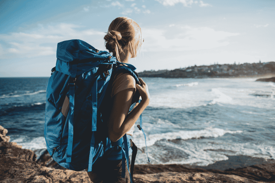 Mulher mochileira observando o mar com mochila azul