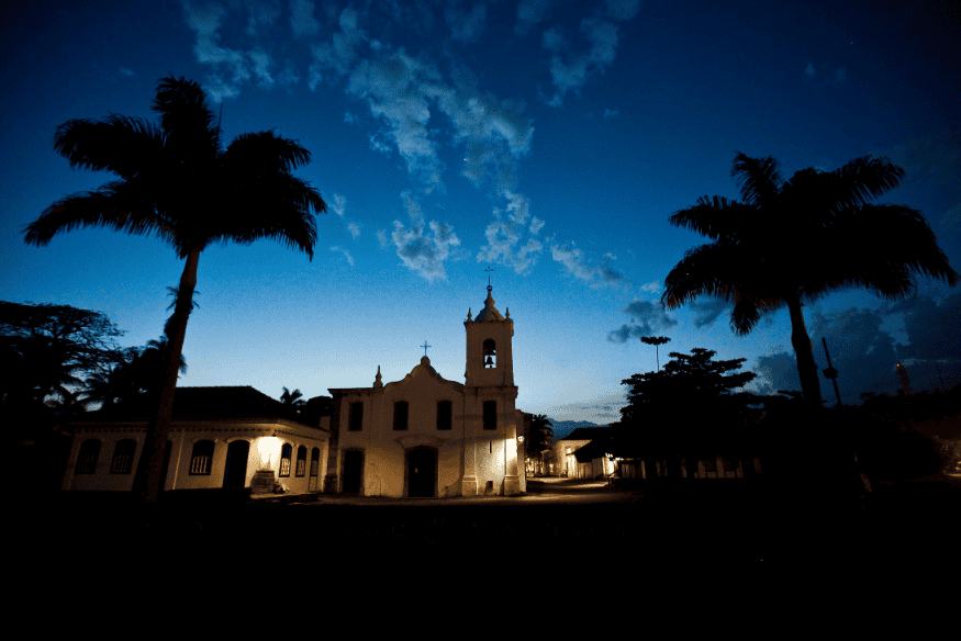 Igreja colonial iluminada ao entardecer com coqueiros em Paraty, Rio de Janeiro