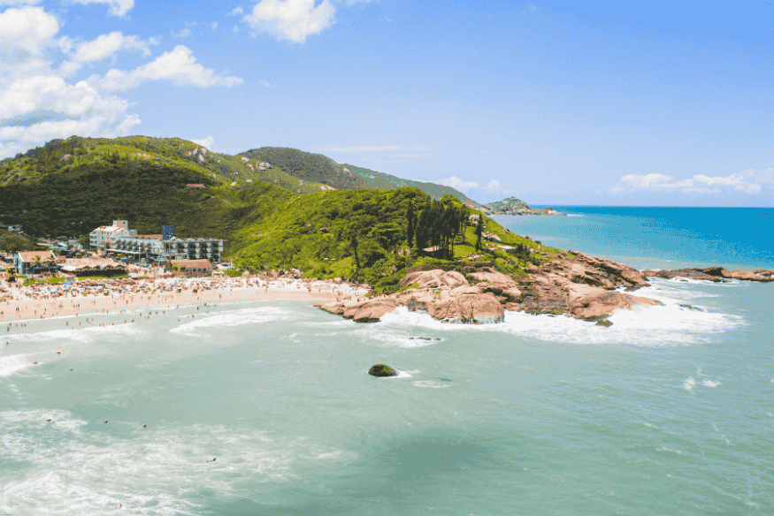 Praia do Santinho em Florianópolis com mar agitado, areia clara e falésias verdes ao fundo.