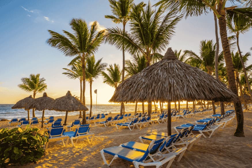 Fileira de espreguiçadeiras e palmeiras na praia de resort all inclusive em Punta Cana ao pôr do sol