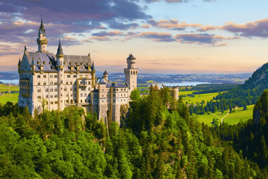 Vista clara do Castelo Neuschwanstein com céu azul e paisagem rural ao fundo.