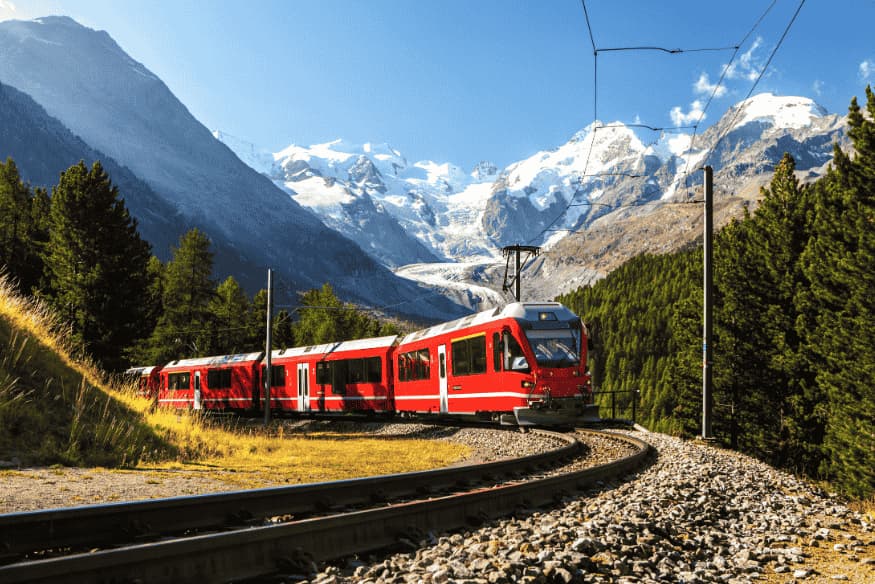 Trem vermelho cruzando trilhos nos Alpes com montanhas cobertas de neve ao fundo