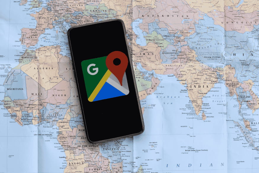 Smartphone com ícone do Google Maps sobre um mapa-múndi.