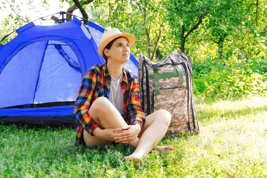 Viajante sentado no gramado ao lado de mochila e barraca.