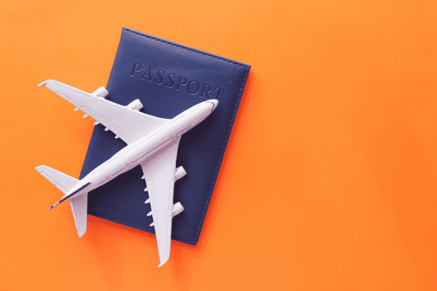 Miniatura de avião sobre capa de passaporte azul em fundo laranja.