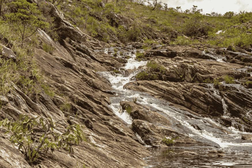 Trilha com riacho em meio a rochas e vegetação na Serra do Cipó