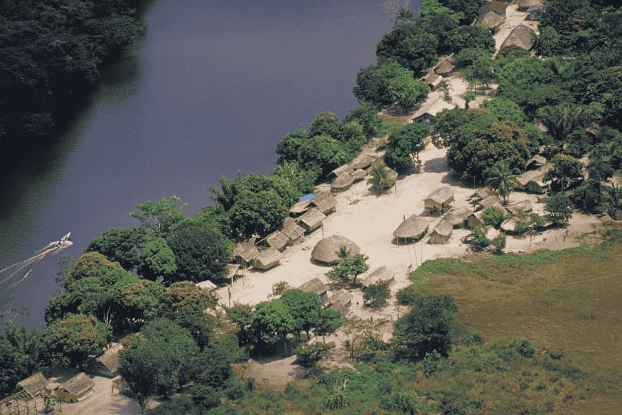Vista aérea de aldeia ribeirinha cercada por floresta e rio na Amazônia.